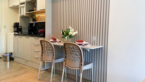Een compacte keuken met eethoek, uitgevoerd in een modern design met een verticale paneelwand, een kleine eettafel, twee stoelen en een vaas met bloemen.