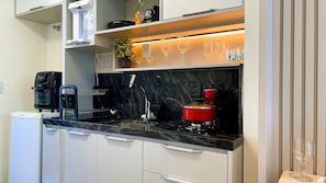 Une cuisine moderne équipée d’une machine à café, d’une bouilloire, d’une casserole rouge et de verres à vin rangés sur une étagère.
