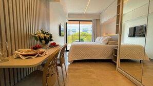 Een hotelkamer met een bed, een bureau met een bloevas, een stoel en een grote spiegel.