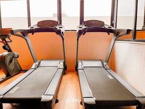 Two treadmills in a gym with wooden flooring and a tiled wall. - OCEAN - STUDIO COM VARANDA - By Living (João Pessoa)