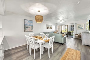 A dining area with a white table and chairs, a woven pendant light, and a view through a glass door to an outdoor area. - Newly Rehabbed • Pickleball/Tennis • Beach Access (Bradenton Beach)
