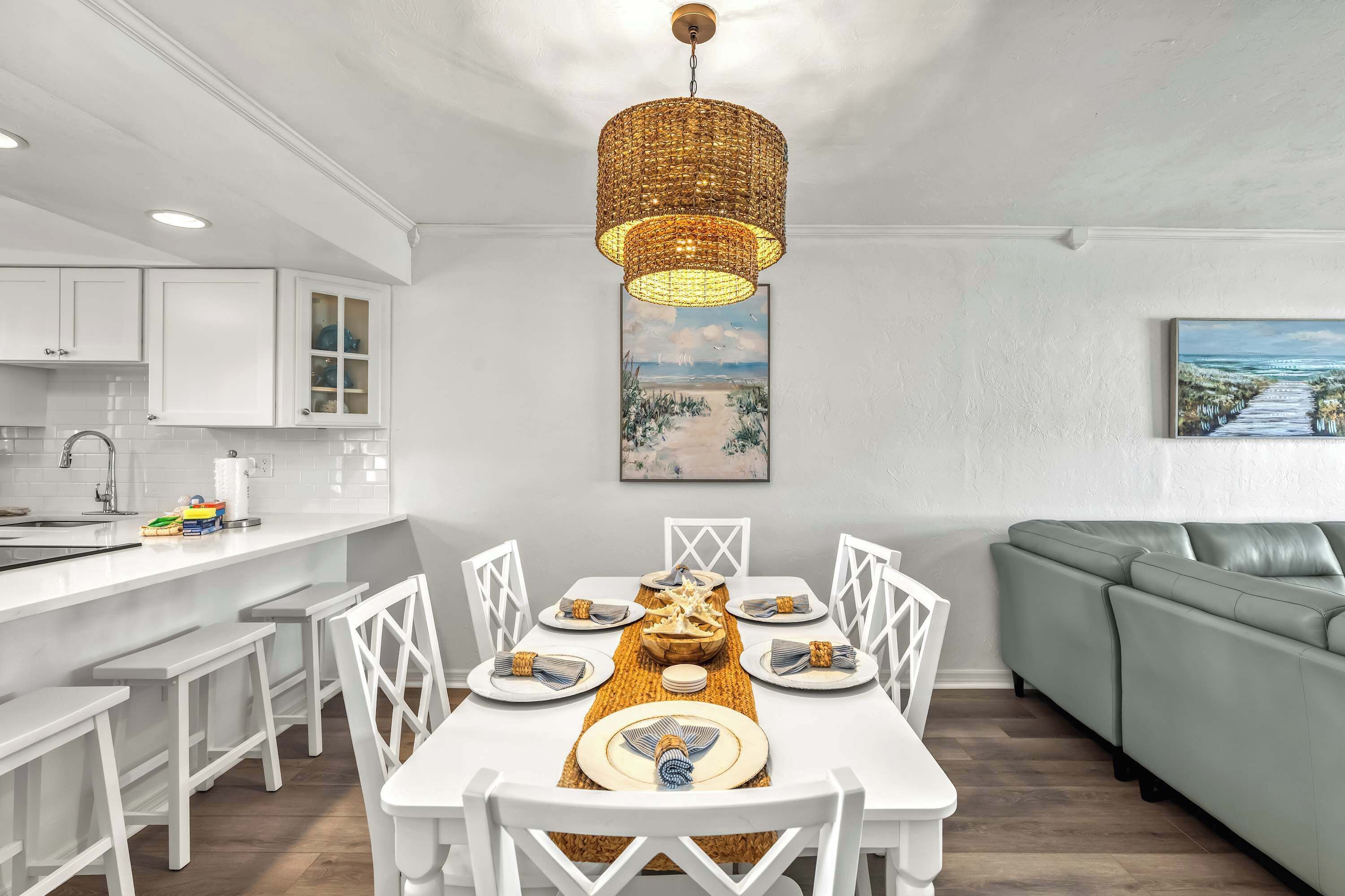 A modern kitchen with white cabinetry, a dining area with a white table set for six, and a green sofa in the living area.