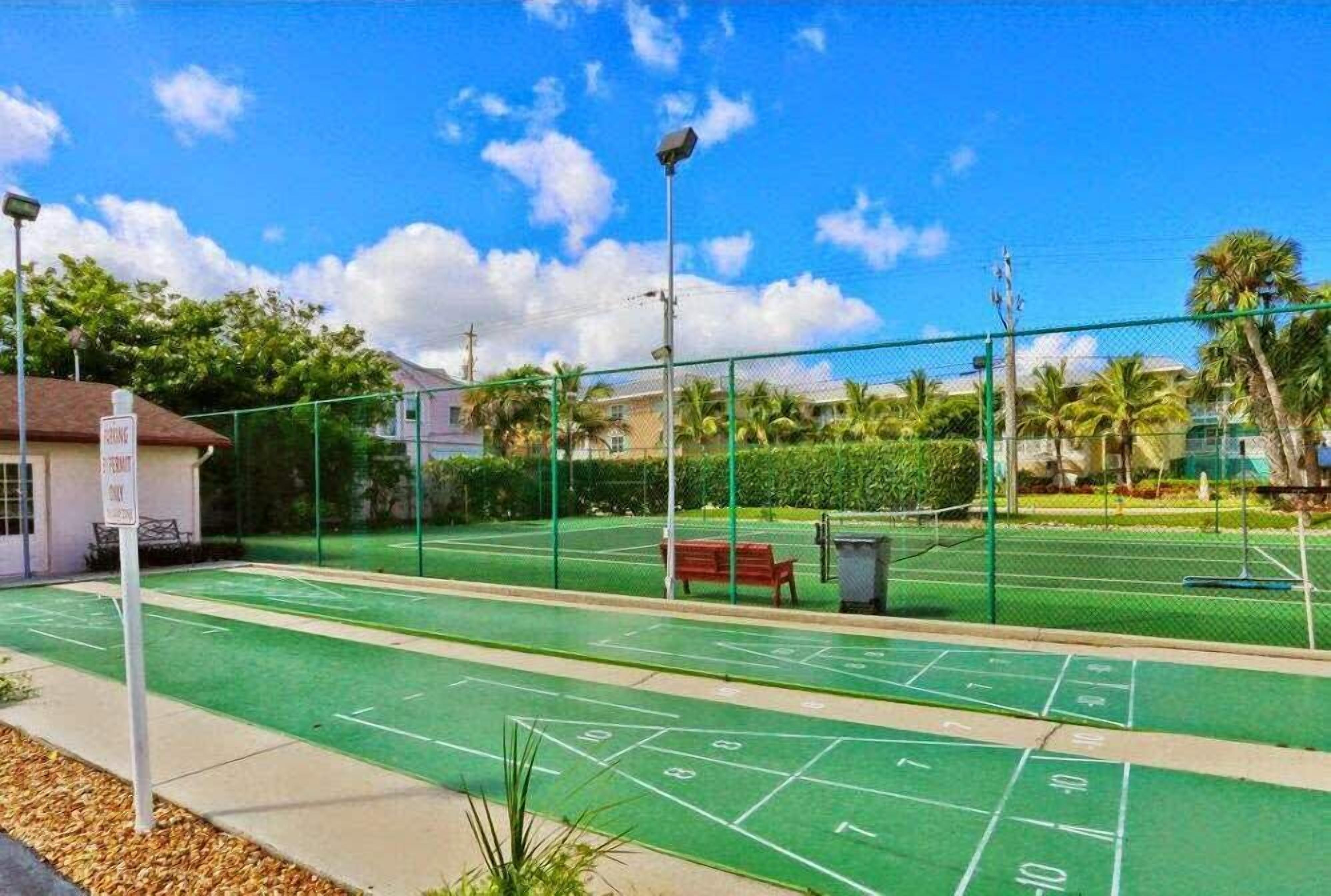 Una cancha de shuffleboard verde al aire libre con valla, banca y contenedor de basura.