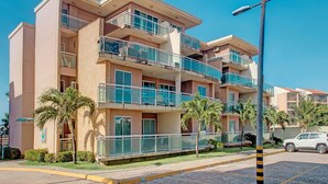 A multi-story hotel with balconies, palm trees, and a paved street. - Palm Beach #201 - Porto das Dunas por Carpediem (Aquiraz)