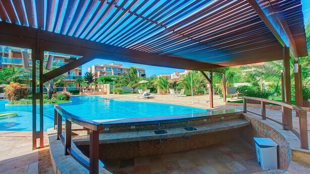 A pool area with a covered seating area and a view of surrounding buildings. - Palm Beach #201 - Porto das Dunas por Carpediem (Aquiraz)