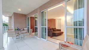 A spacious balcony with a dining area, a sofa, and a view of the interior. - Palm Beach #201 - Porto das Dunas por Carpediem (Aquiraz)