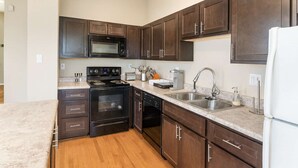 A kitchen with dark wooden cabinets, a stainless steel sink, a microwave, an oven, and a dishwasher.