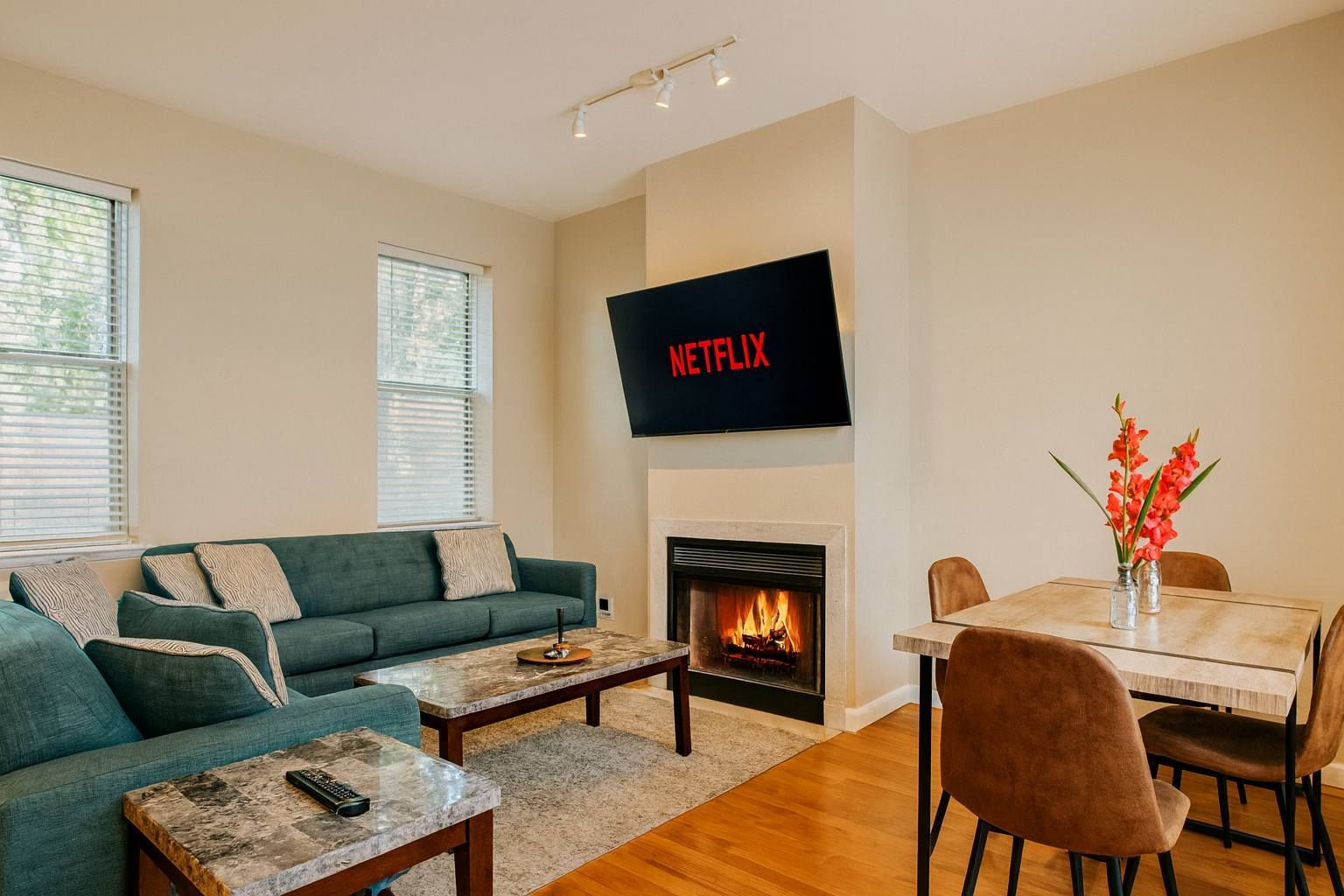 Ein Wohnzimmer mit einem grünen Sofa, einem Couchtisch, einem Kamin, einem Esstisch mit Stühlen und einem Fernseher, der über dem Kamin angebracht ist.