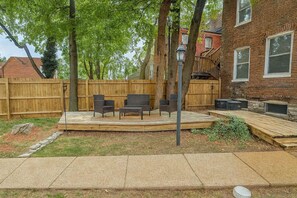 A backyard with a wooden deck, outdoor furniture, and a brick building in the background. - Pet-Friendly Soulard 2BR with Parking (St. Louis)