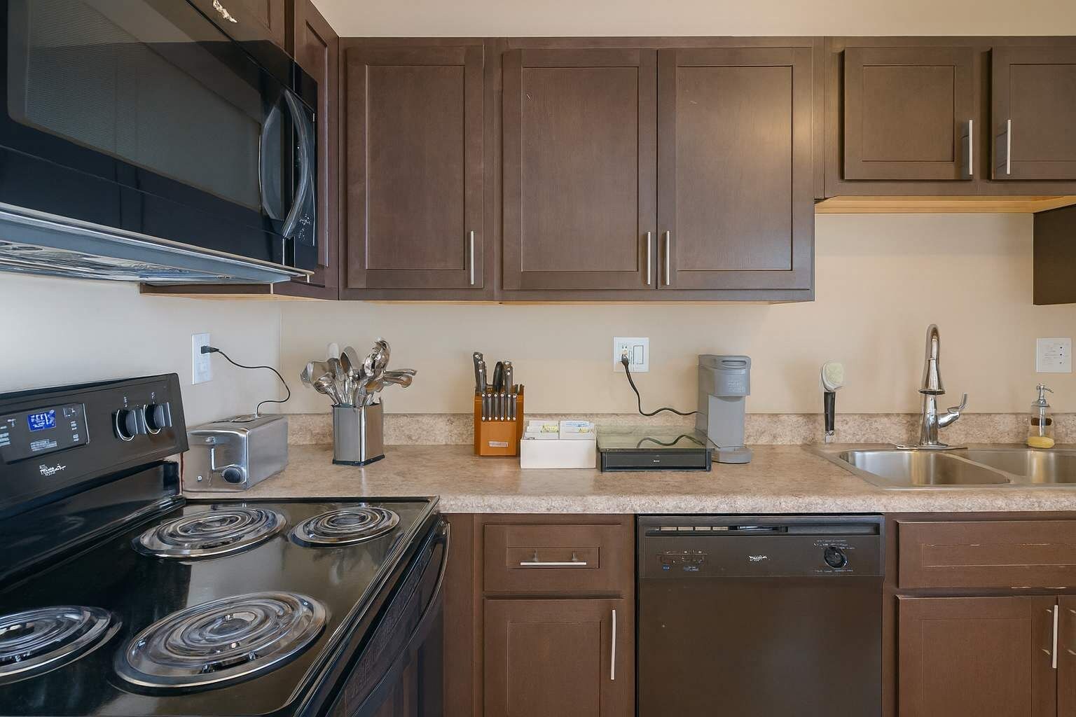 A modern kitchen with dark wooden cabinets, a black stove, a dishwasher, and a coffee maker.