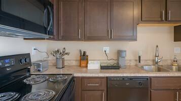 A modern kitchen with dark wooden cabinets, a black stove, a dishwasher, and a coffee maker.