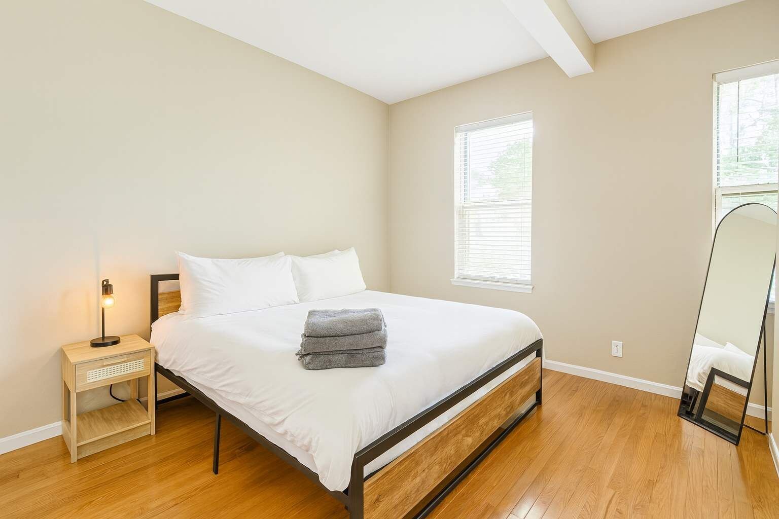 Quarto com cama, mesa de cabeceira, abajur e um espelho grande.