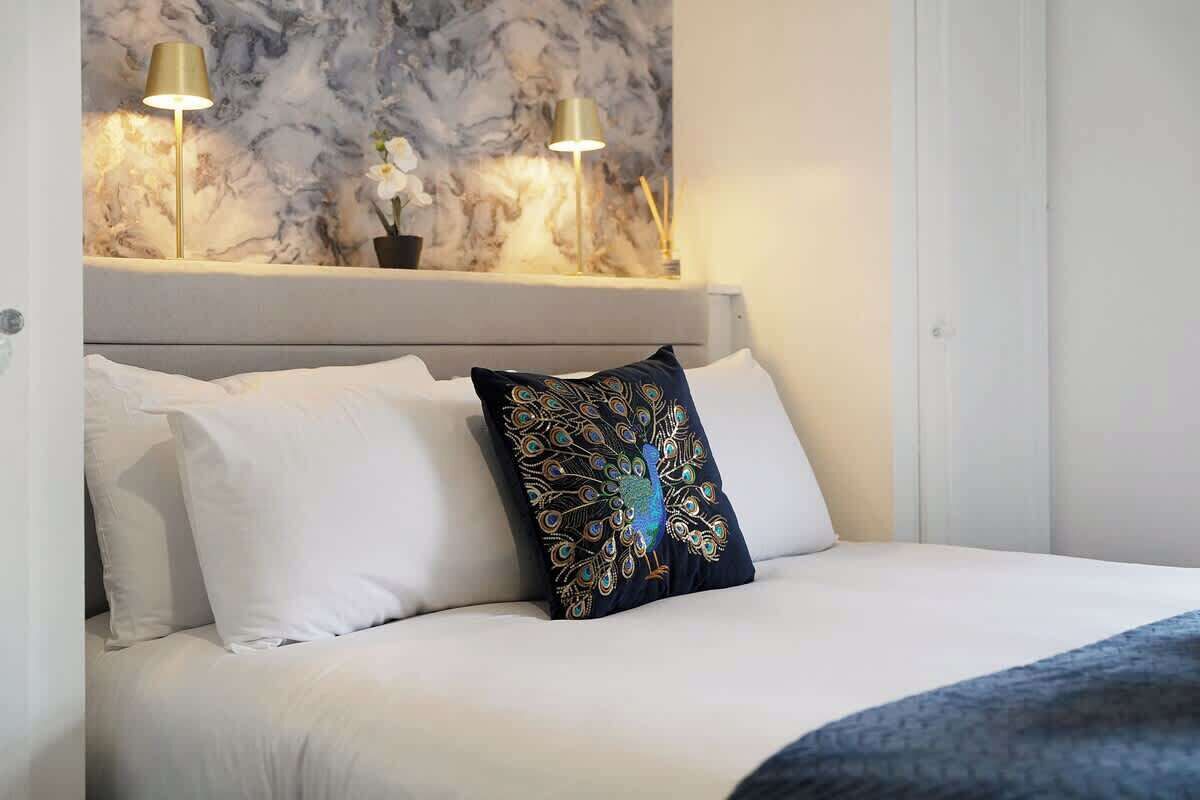 A bed with white bedding, a decorative pillow, and two wall-mounted lamps.