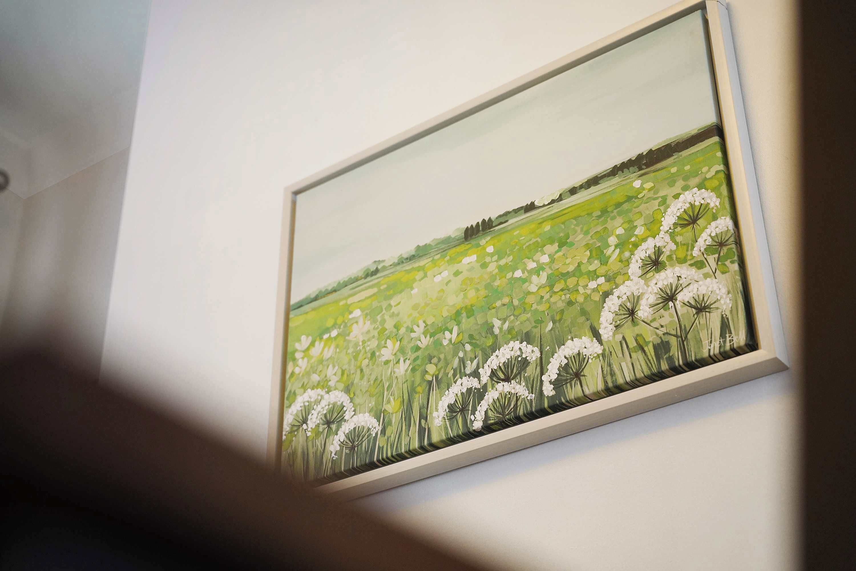 Un tableau encadré représentant un champ parsemé de fleurs blanches, accroché à un mur.