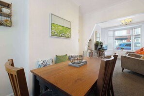 Uma sala de jantar com uma mesa de madeira, cadeiras, uma tigela decorativa, um quadro e vista para o exterior através de uma janela.