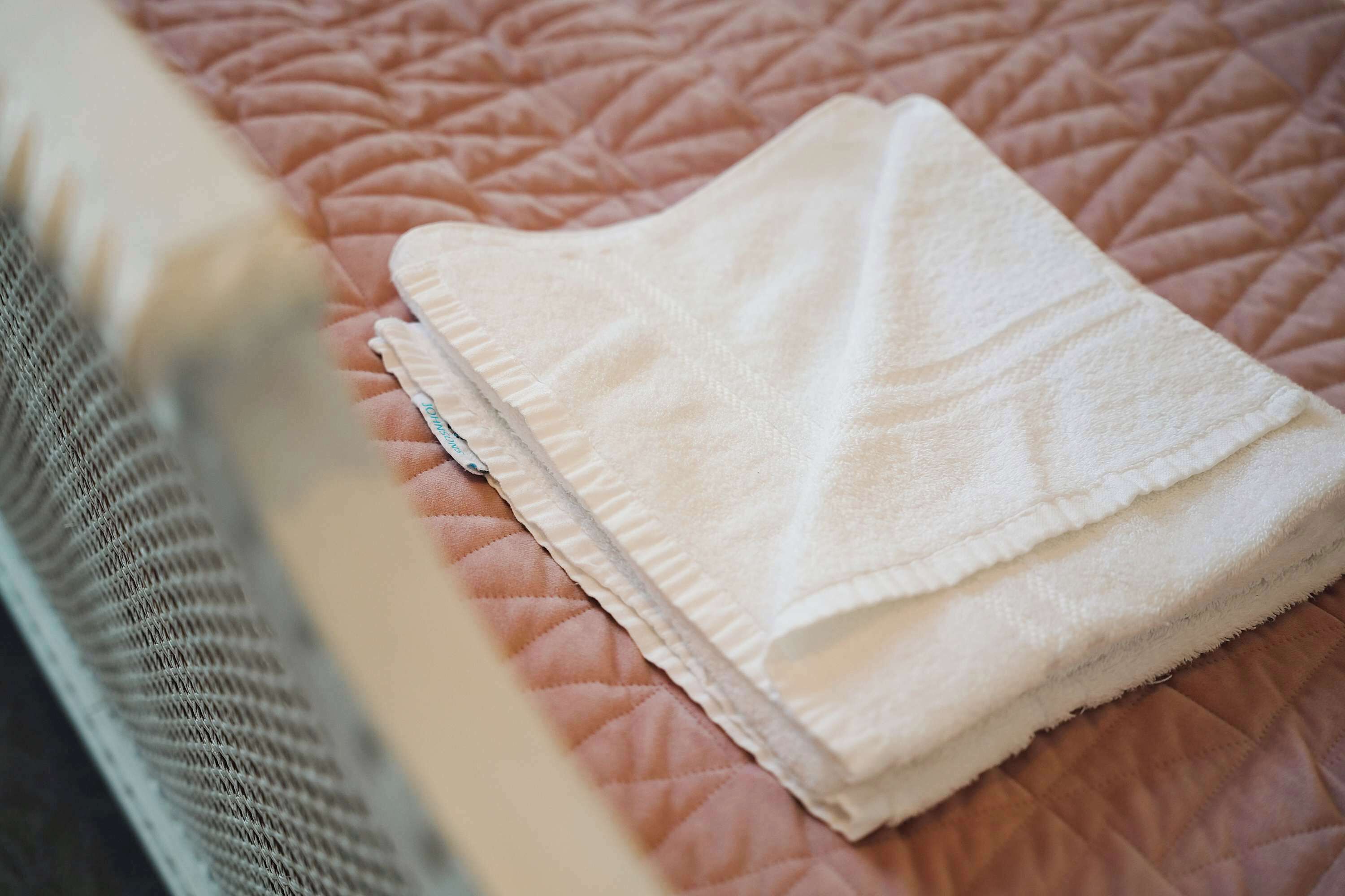 A neatly folded white towel on a pink quilted bedspread.