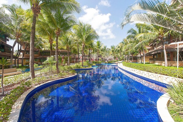 Una piscina de diseño curvo, rodeada de palmeras y un cielo azul despejado.