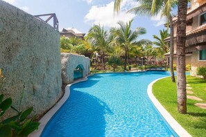 A swimming pool with a curved edge, surrounded by palm trees and a building with a thatched roof. - Parque das Ilhas #102 - Excellence by Carpediem (Aquiraz)
