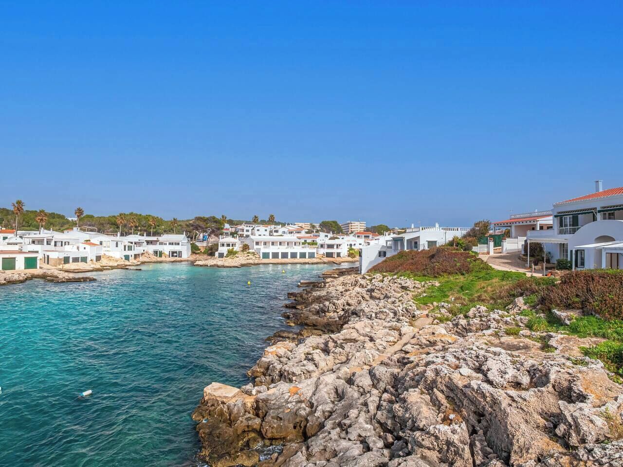 Une ville côtière aux bâtiments blancs qui bordent le front de mer, avec un littoral rocheux et une mer d’un bleu limpide.