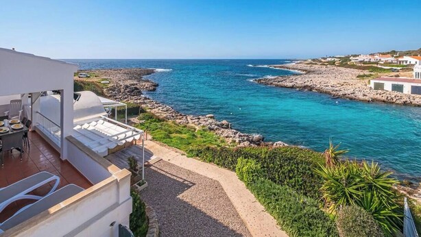 Uma propriedade costeira com terraço com vista para a costa rochosa e águas azul-claras.