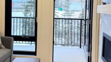 A modern living room with a grey sofa, a coffee table, and a large window with a view of a snowy landscape.