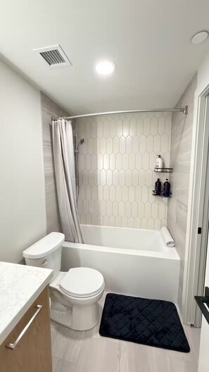 A modern bathroom with a toilet, bathtub, and shower. - Canmore Peaks Retreat | Luxe 1BR w Pool & Gym (Canmore)