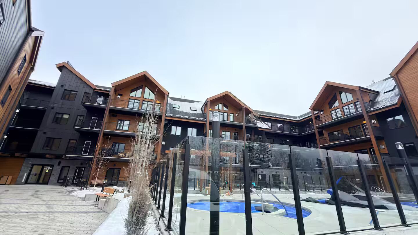 A multi-story building with balconies, a central courtyard with a pool, and a clear sky.
