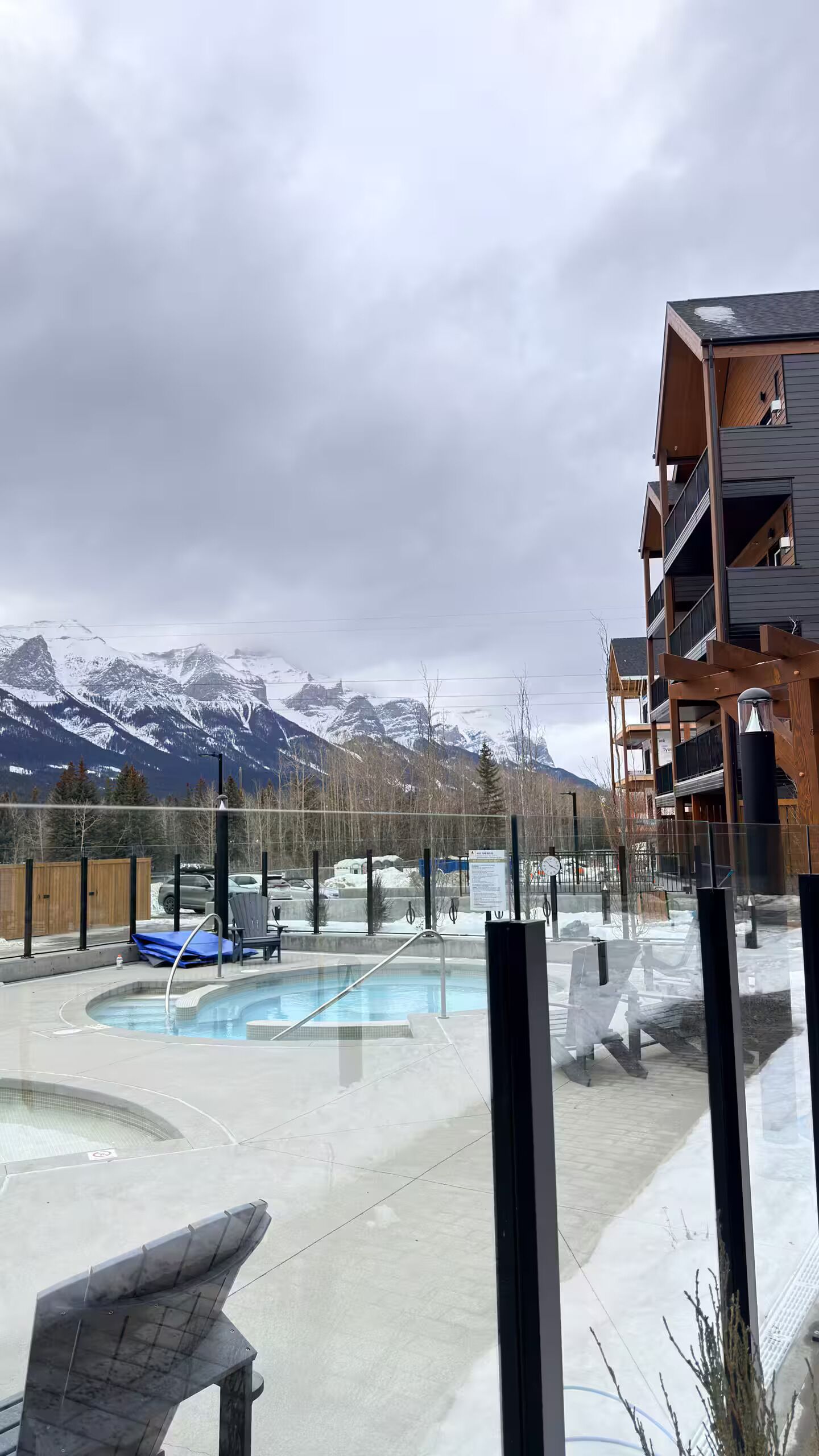 A pool area with a view of snow-capped mountains, a wooden deck, and a modern building with balconies.