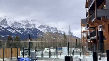A pool area with a view of snow-capped mountains, a wooden deck, and a modern building with balconies.