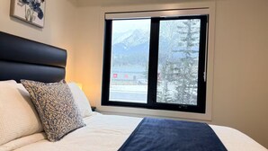 Un dormitorio con cama, almohadas y ventana con vista a la montaña.