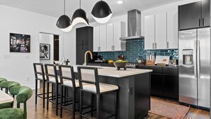 A modern kitchen with black and white cabinetry, a central island with bar stools, and a stainless steel refrigerator. - Sleeps 20: Views, HotTub, FirePit, Grill, Parking (Nashville)
