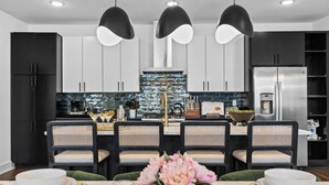 A modern kitchen with black and white cabinetry, a central island with a sink, and a stainless steel refrigerator. - Sleeps 20: Views, HotTub, FirePit, Grill, Parking (Nashville)