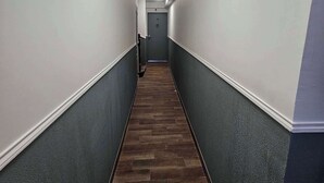 Un couloir étroit doté d’un plancher en bois foncé et de murs aux couleurs contrastées, claires et foncées.