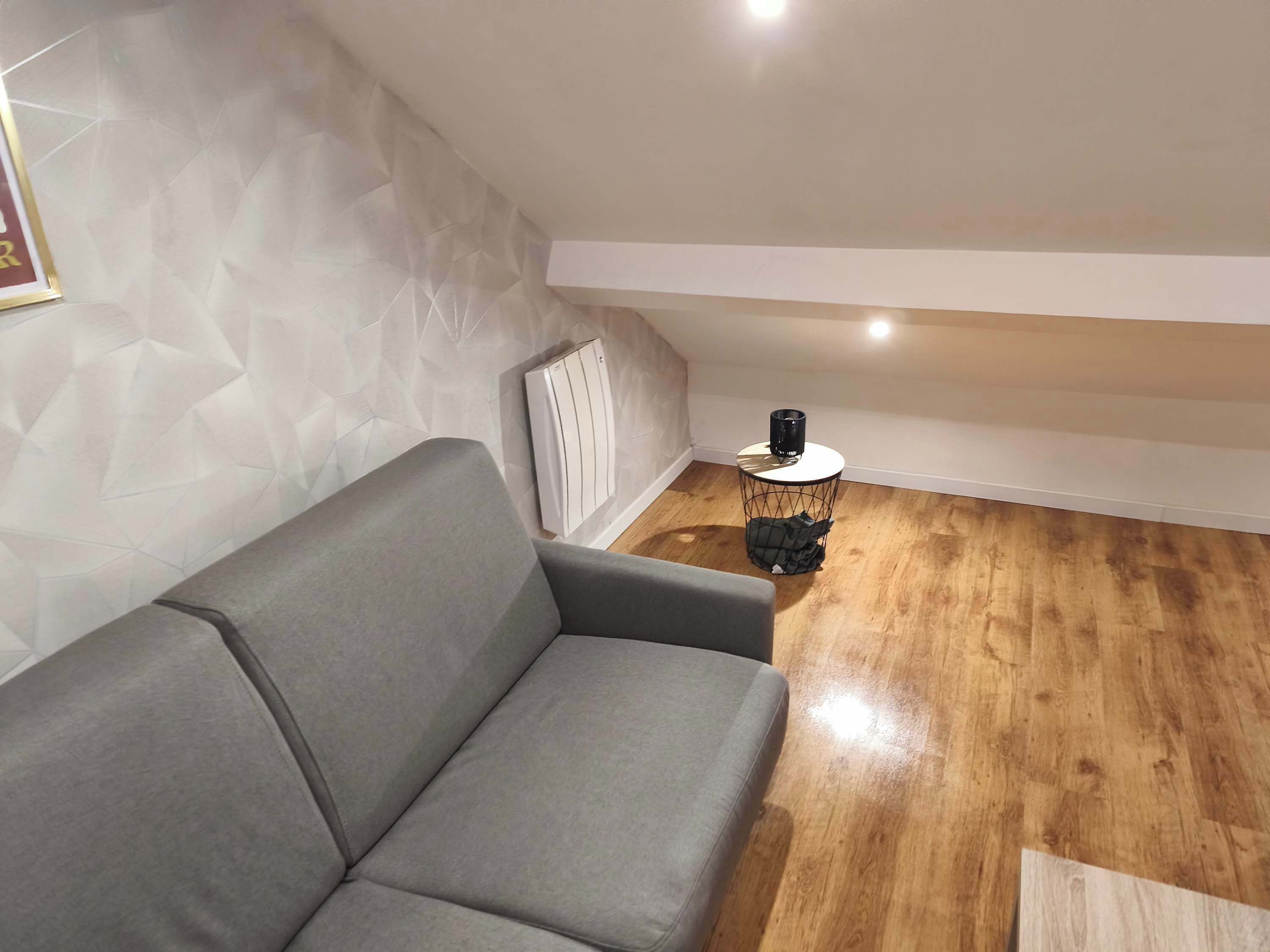Una sala moderna con un sofá gris, una mesita redonda con un objeto negro y una pared con estampado geométrico.