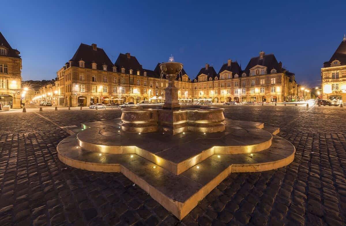 Una plaza histórica con una fuente en el centro, adoquinado y edificios iluminados.