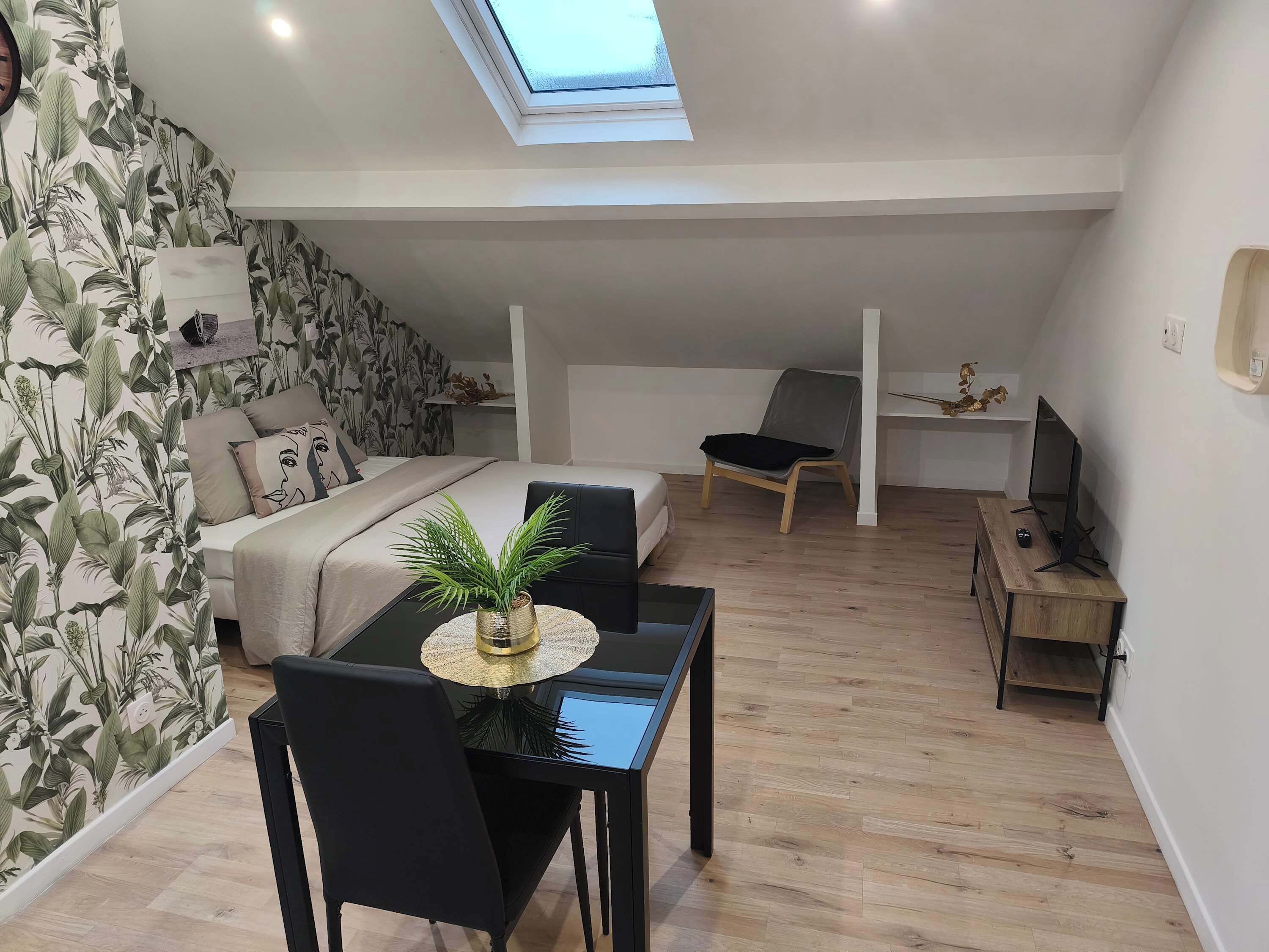 Un dormitorio tipo loft moderno con tragaluces, una cama con cabecera, una mesa de comedor con sillas y un televisor sobre un mueble de madera.