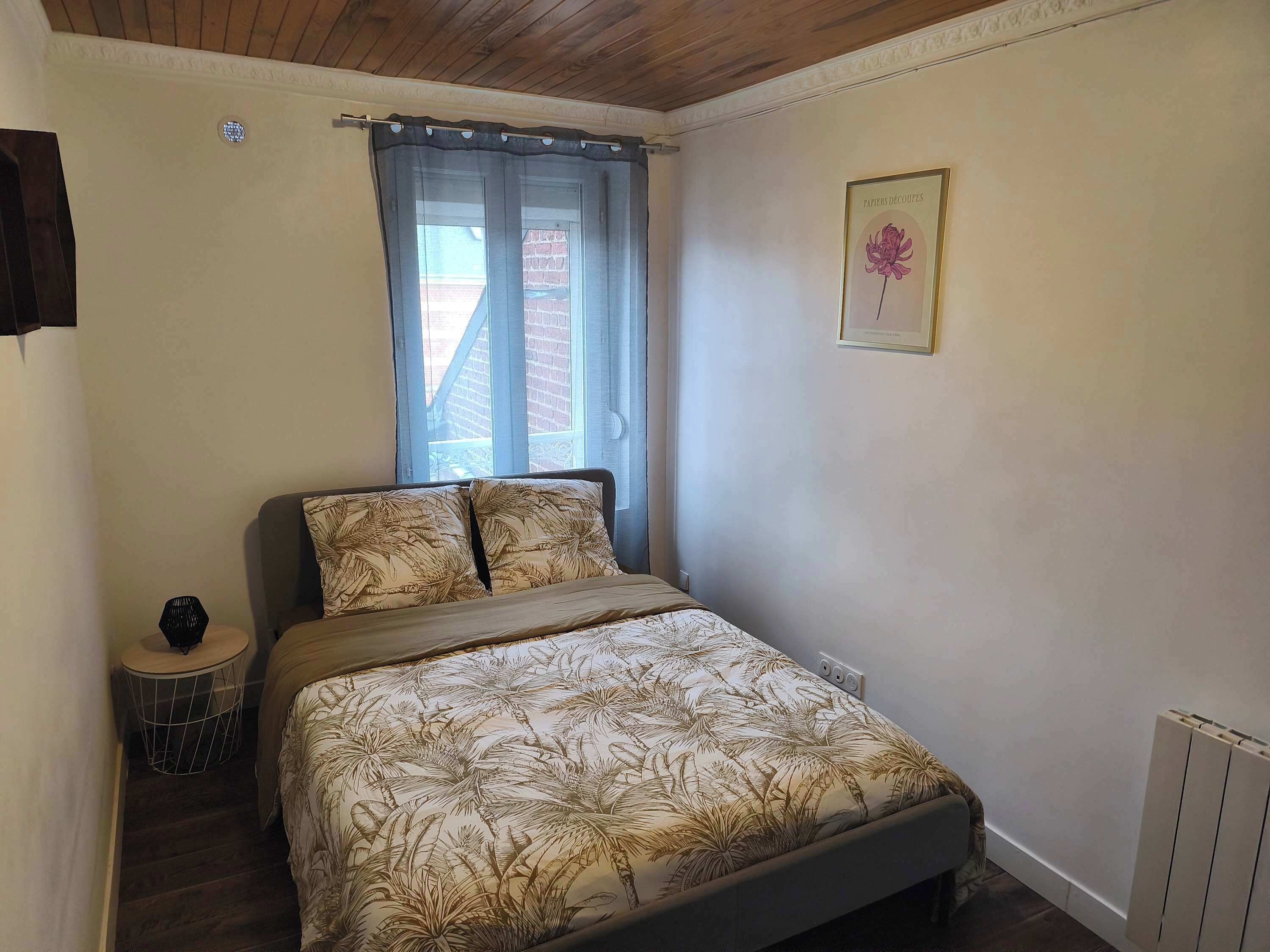 Une chambre avec un lit, une fenêtre avec des rideaux, une petite table ronde et un radiateur.
