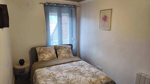 Ein Schlafzimmer mit Bett, einem Fenster mit Vorhängen, einem kleinen runden Tisch und einem Heizkörper.