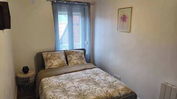 Une chambre avec un lit, une fenêtre avec des rideaux, une petite table ronde et un radiateur.