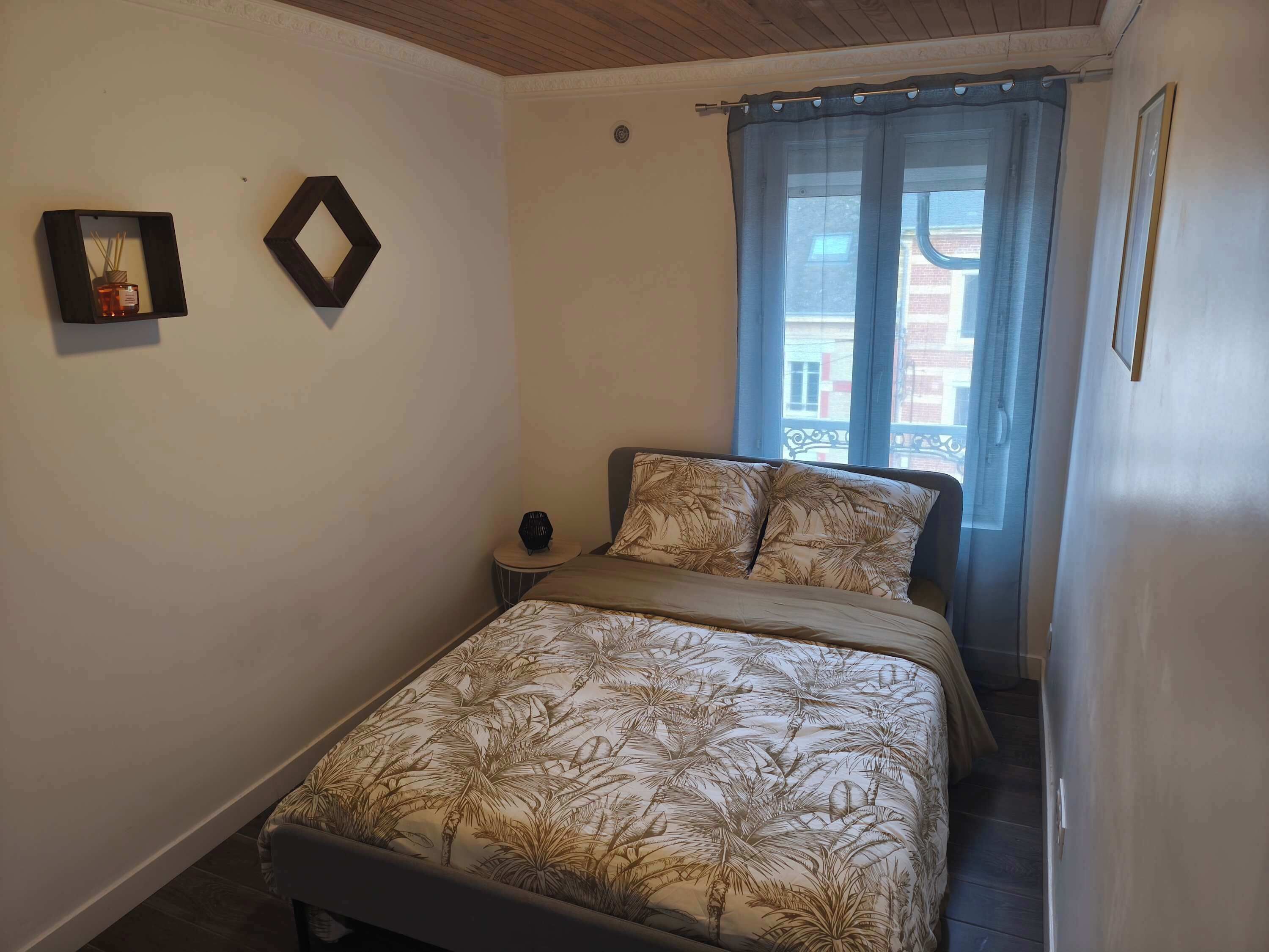 Une chambre à coucher comprenant un lit, une table de chevet, une fenêtre avec des rideaux et deux cadres photo accrochés au mur.