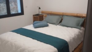 Ein Schlafzimmer mit einem Bett, einem Nachttisch, einer Lampe und einem Fenster.