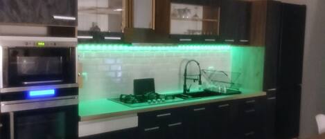 A modern kitchen with built-in ovens, a green-lit island, and dark cabinetry.