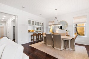 A modern kitchen with white cabinetry, a dining area with a table and chairs, and a large mirror above the table.