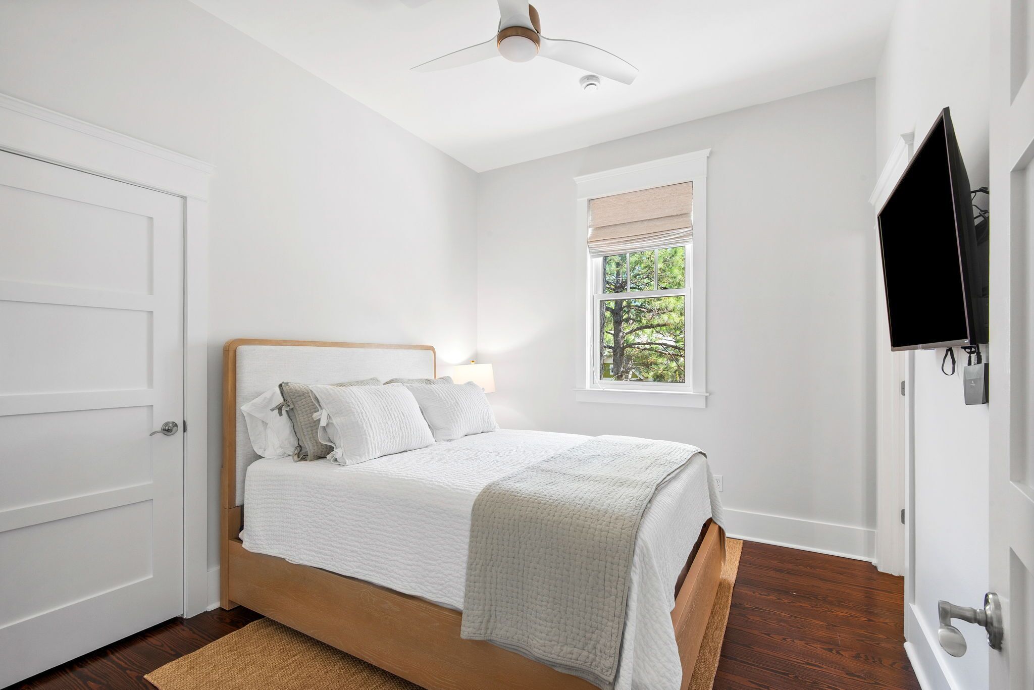 Un dormitorio con cama, ventana con vistas, ventilador de techo y televisor montado en la pared.