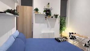 Une chambre à coucher avec un lit, une chaise, une petite table et des étagères avec des plantes.