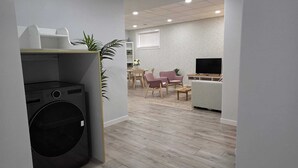 Una sala de estar moderna con televisor de pantalla plana, un comedor con mesa y sillas, y una cocina con lavadora.