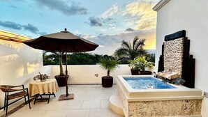 Une terrasse sur le toit avec un jacuzzi, des plantes en pot, une table avec des chaises et un parasol.
