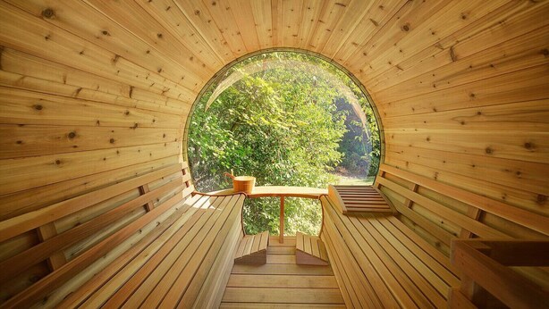 A wooden interior with a circular window, wooden benches, and a table. - Luxury Wooded Estate With Pool (Sammamish)
