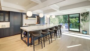 A modern kitchen with a central island, dark cabinetry, and a large window overlooking a garden. - Luxury Wooded Estate With Pool (Sammamish)