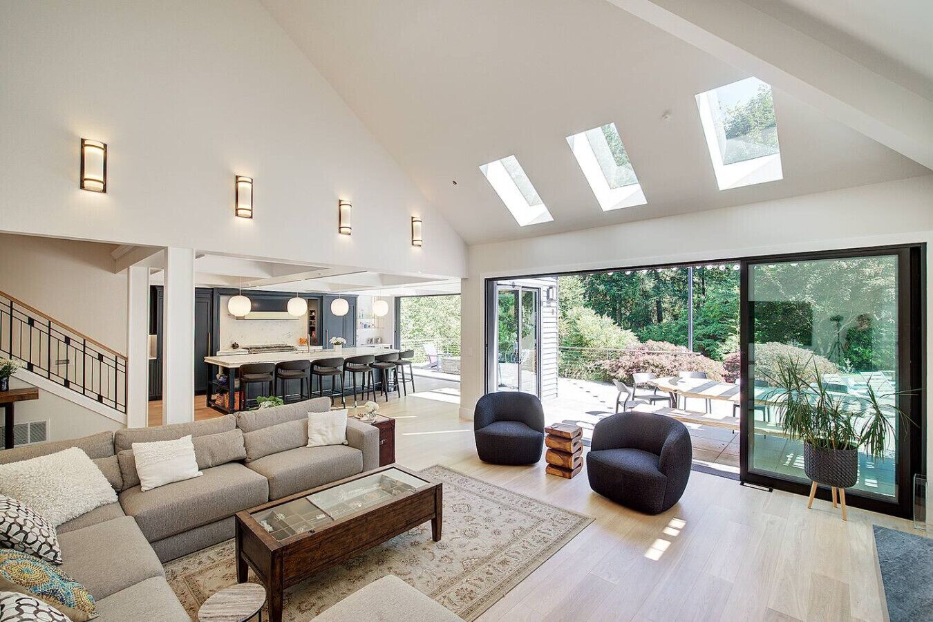 A spacious living area with a large sofa, two armchairs, a coffee table, and a dining area with a kitchen in the background.